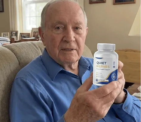 An older man in a blue shirt holding up a Quiet Nerves bottle in a living room armchair